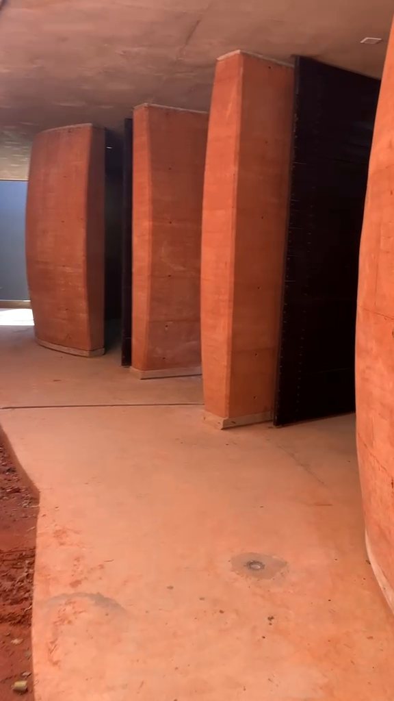Paso entre los muros curvos, con el portón de acceso a los sanitarios