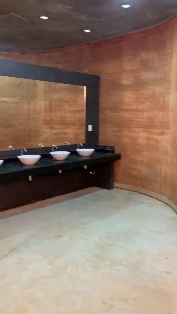 Interior de los sanitarios: mesada con lavatorios y espejo sobre el muro curvo
