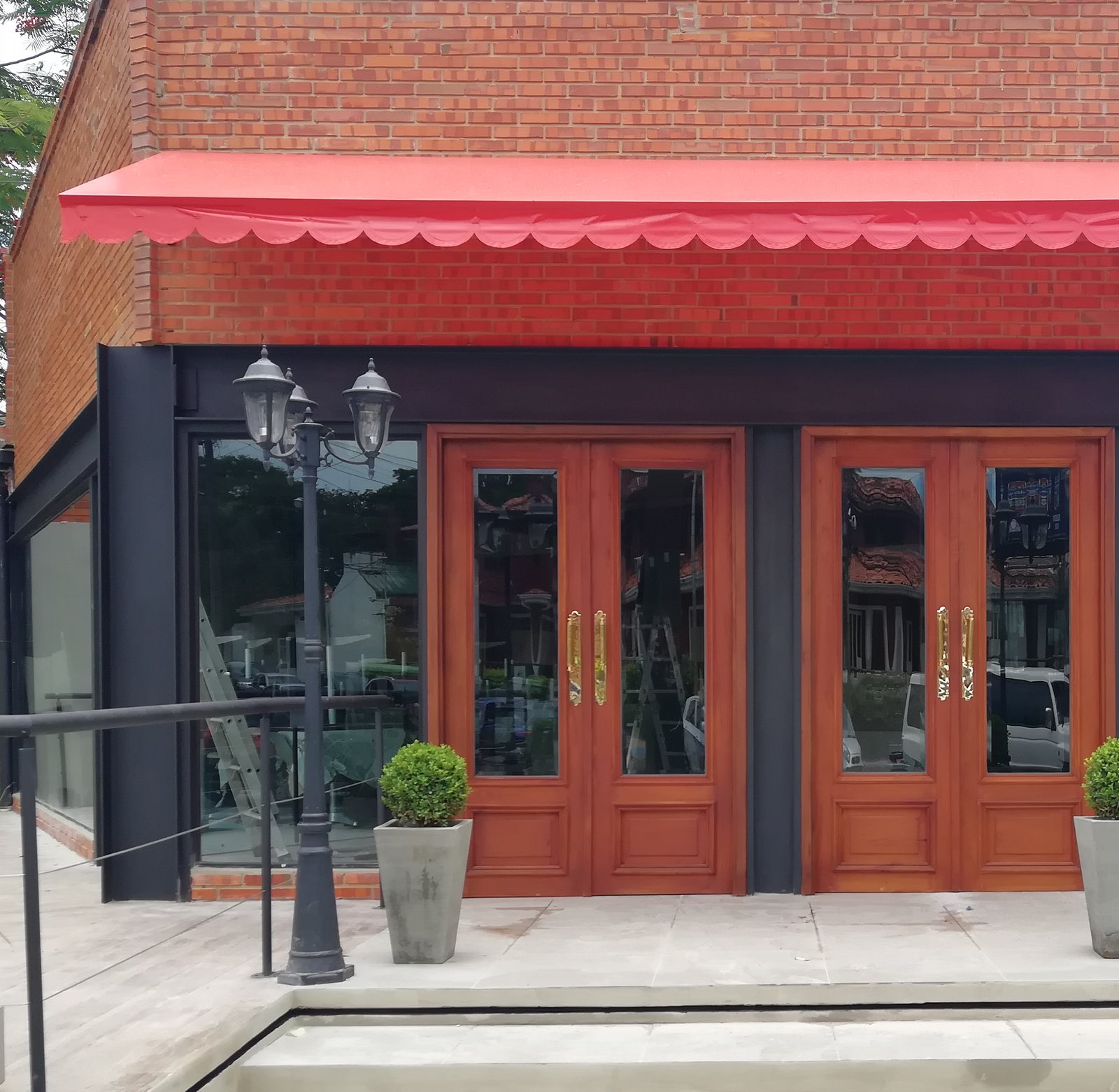 Frente de un local con estructura metálica negra, puertas de madera, faroles y toldo rojo