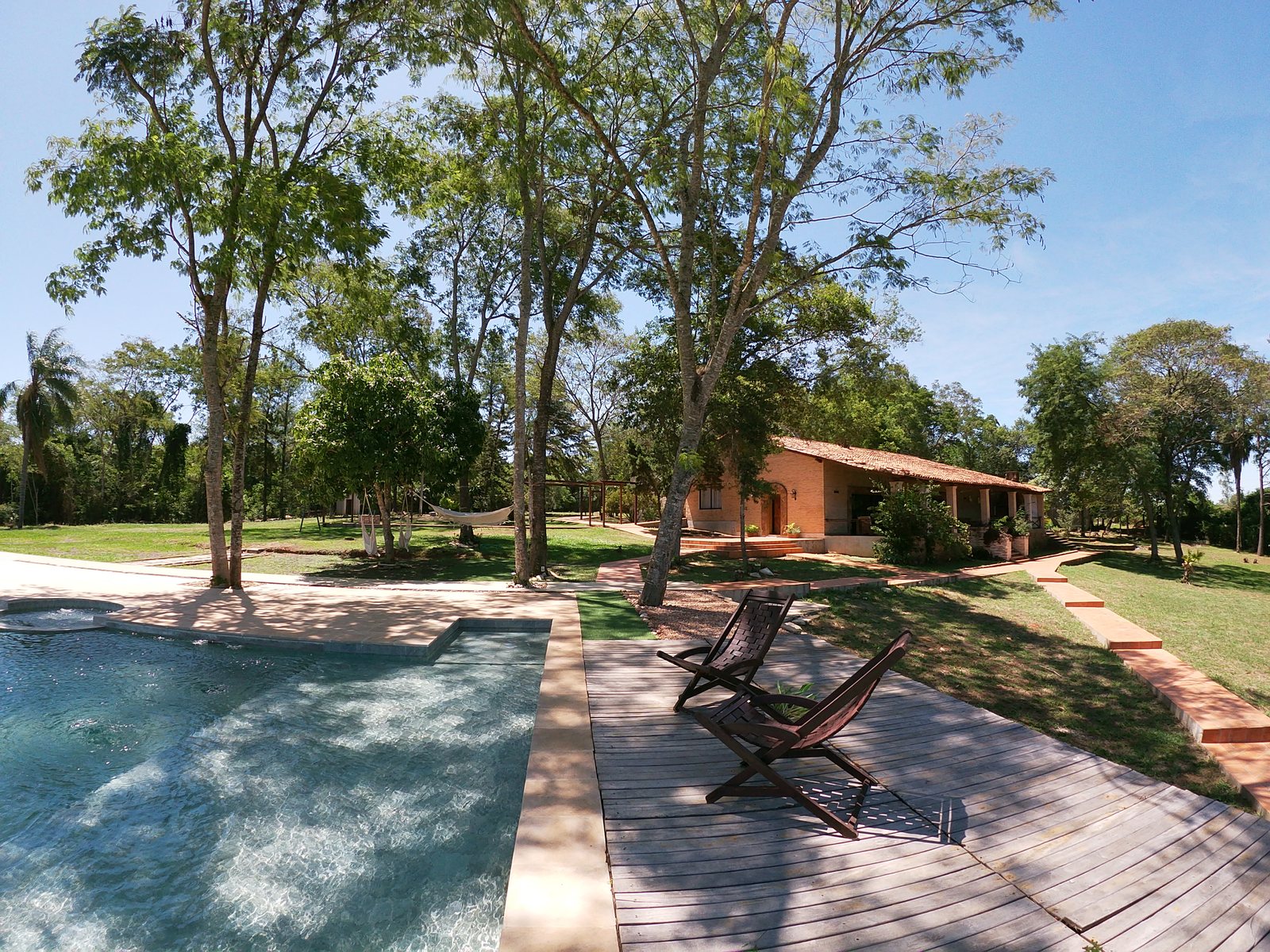 Esquina de la piscina con el deck de madera, el parque y la casa