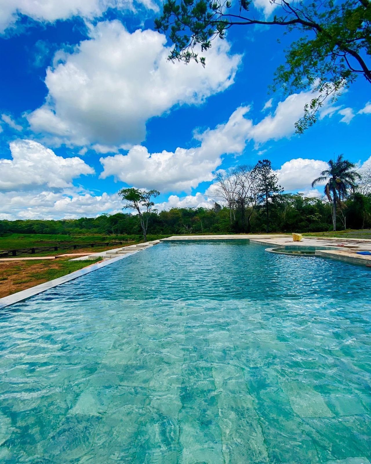 Piscina de Ára Lodge terminada, con agua, revestimiento y borde infinito frente al parque