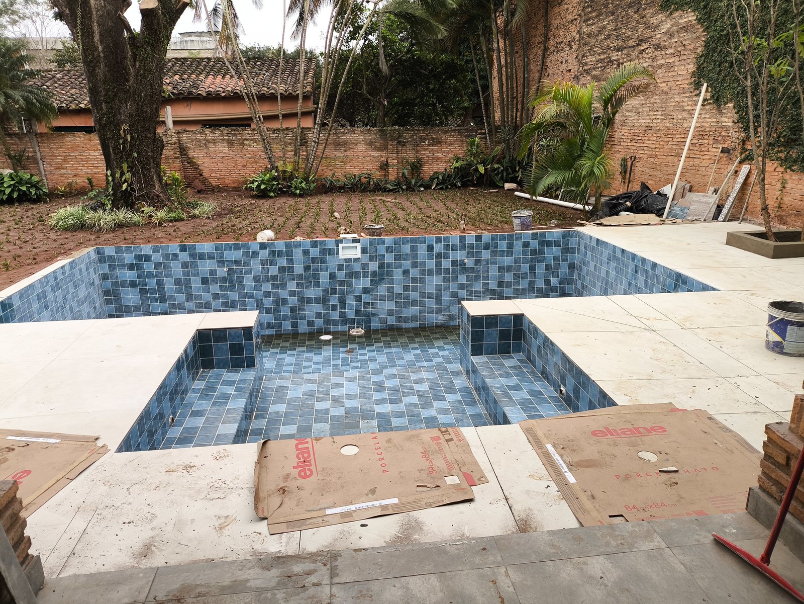 Piscina revestida con piezas azules y solárium de losetas claras, antes del llenado