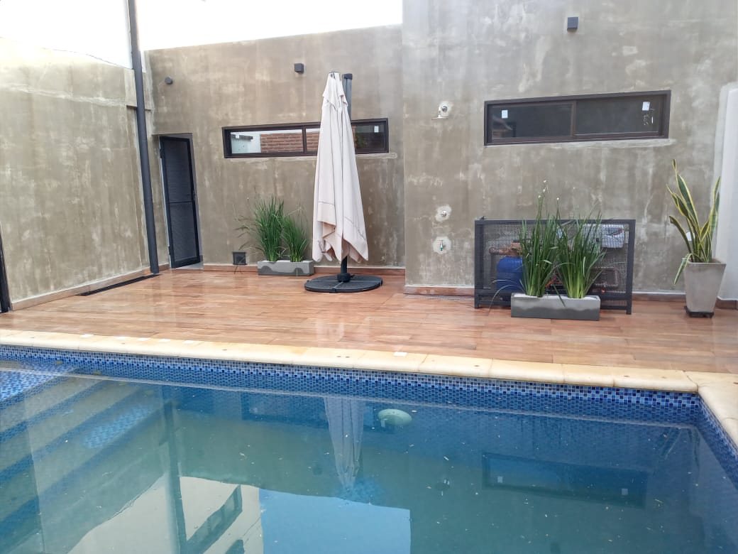 Piscina revestida con venecitas azules, con borde claro y solárium en tono madera