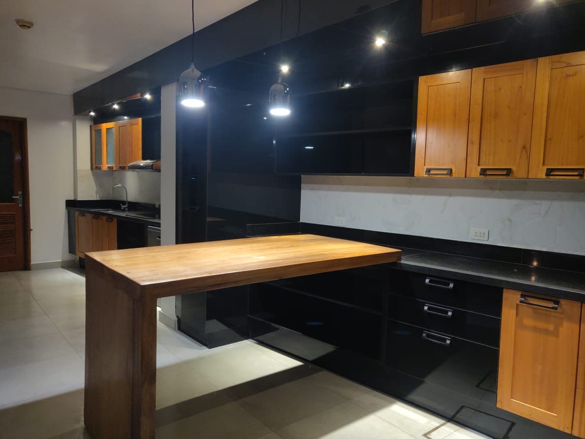 Cocina con muebles negros y de madera, barra y luminarias colgantes