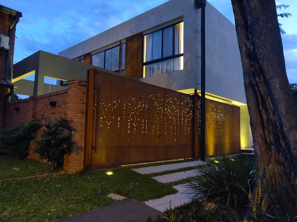 Vivienda de dos plantas con cerramiento de acero corten perforado, iluminada al anochecer