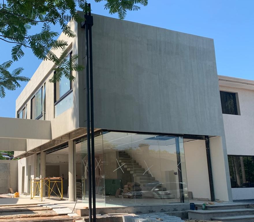 La fachada en obra: volumen superior de hormigón y planta baja vidriada, con la escalera a la vista